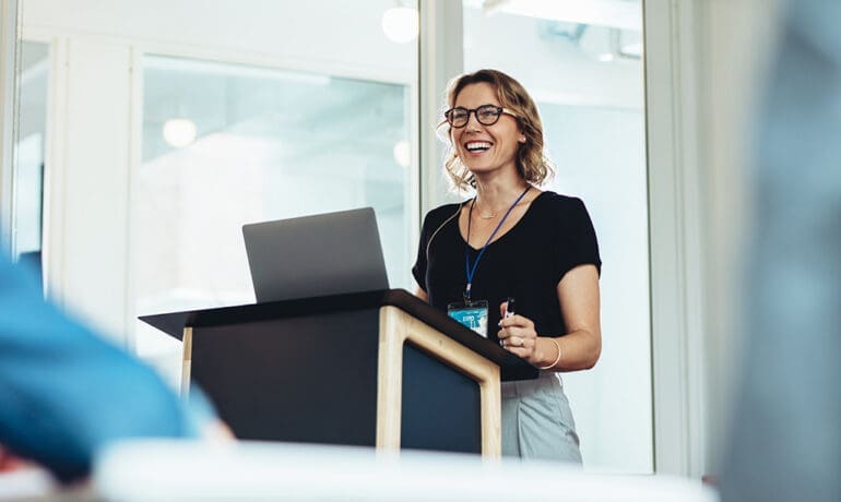 Businesswoman standing at podium with laptop giving a speech. Successful female business professional addressing a seminar.